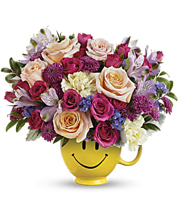 Cheerful smile face flower arrangement in a yellow smiley mug filled with vibrant roses and colorful flowers.