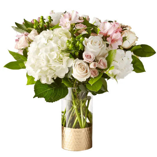 Romantic spring flower bouquet featuring white hydrangeas, pink roses, and greenery in a glass vase.